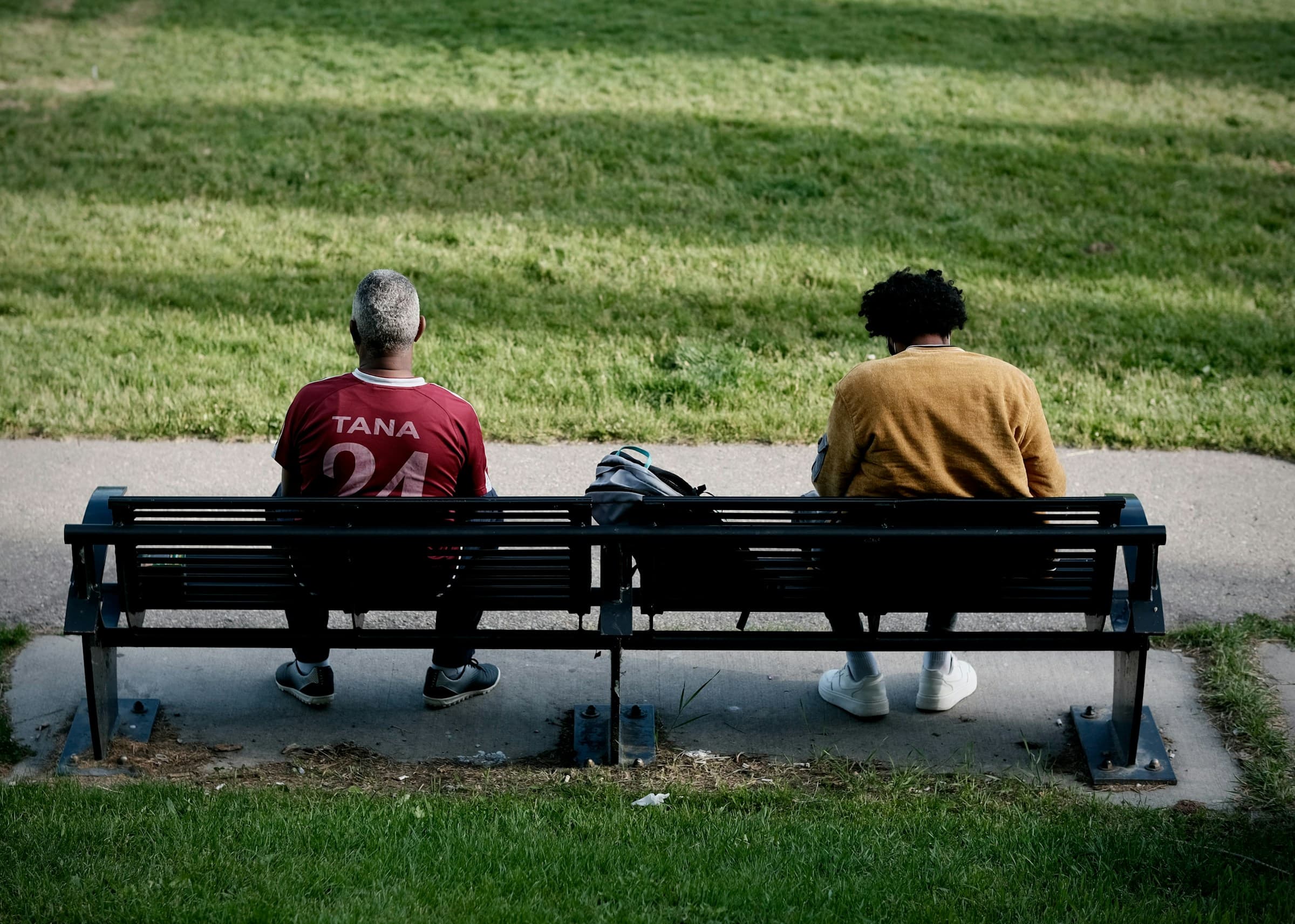 Twee mensen zitten naast elkaar op een bank in het park, van achteren gezien.